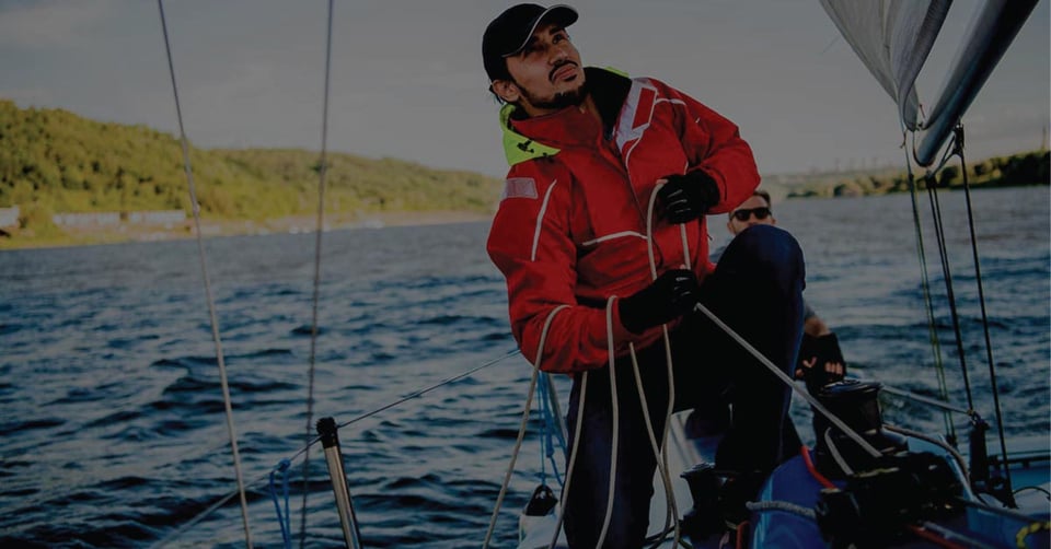 Sailor adjusting ropes on a sailboat with a teammate behind him