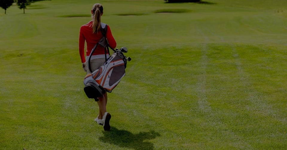 Golfer carrying a golf bag while walking the course